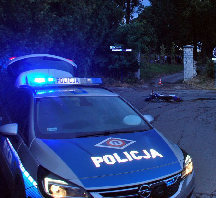 Fotografia kolorowa. Na zdjęciu na pierwszym planie widoczny radiowóz, z kolei w oddali widać leżący na jezdni motocykl. 