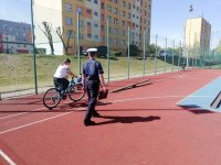 Fotografia kolorowa. Na zdjęciu widoczny policjant nadzorujący przejazd dziecka na rowerze.