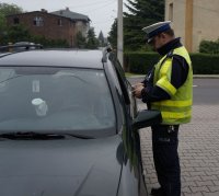 Fotografia kolorowa. Na zdjęciu widoczny policjant przeprowadzający kontrolę drogową.