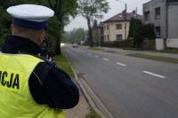 Fotografia kolorowa. Na zdjęciu widoczny stojący tyłem policjant wykonujący pomiar prędkości pojazdu.