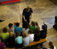 Fotografia kolorowa. Policjantka daje dzieciom mikrofon, żeby mogły zadać pytanie do przybyłych gości.