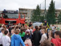 Fotografia kolorowa. Na zdjęciu widać radiowóz policyjny oraz wóz strażacki. Przy pojazdach znajdują się dzieci.