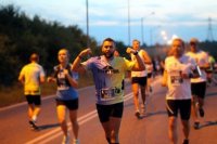 Fotografia kolorowa. Na zdjęciu widoczny policjant biorący udział w biegu w otoczeniu zawodników.