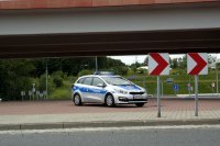 Fotografia kolorowa. Na zdjęciu widoczny radiowóz stojący na rondzie podczas kierowania ruchem przez policjanta.