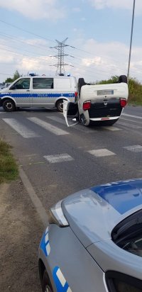 Fotografia kolorowa. Na zdjęciu widoczne dwa radiowozy oraz leżący na dachu citroen.