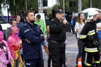 Fotografia kolorowa. Na zdjęciu trwający pokaz służb mundurowych, komentarz policjanta oraz strażaka.