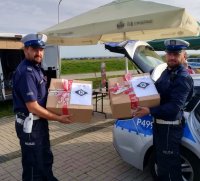 Fotografia kolorowa. Na zdjęciu widoczni policjanci trzymający paczki przeznaczone dla hospicjum.