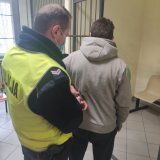 policjant z osobą poszukiwaną w pomieszczeniu dla osób zatrzymanych