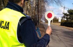 Umundurowany policjant ruchu drogowego trzymający w prawej ręce tarczę do zatrzymywania pojazdów.