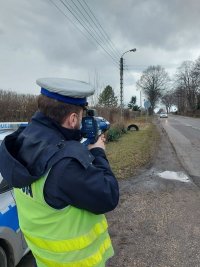 Umundurowany policjant ruchu drogowego dokonujący pomiaru prędkości nadjeżdżającego pojazdu.