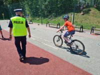 Umundurowany policjant, z boku którego jedzie na rowerze egzaminowany na kartę rowerową