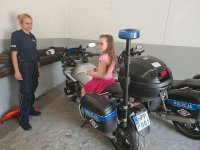 Umundurowana policjantka stojąca obok policyjnego motocykla, na którym siedzi dziewczynka