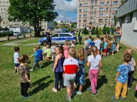 Przedszkolaki stojące na trawie podczas wizyty policjantów rozmawiających o bezpieczeństwie w wakacje