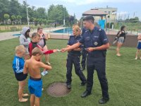 Policjanci wręczający ulotki dzieciom podczas otwarcia basenu.