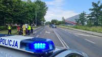 Sygnały świetlne umieszczone na dachu radiowozu policyjnego. w oddali funkcjonariusze Straży Pożarnej oraz Policji podczas oględzin motocykla oraz radiowóz Policji zabezpieczający miejsce zdarzenia.