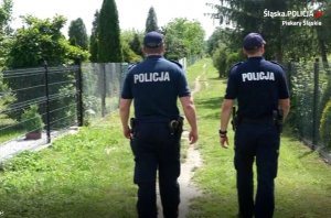 Dwaj umundurowani policjanci podczas pieszego patrolu ogródków działkowych