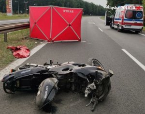 Motocykl leżący na jezdni, z tyłu parawan oraz ambulans pogotowia ratunkowego