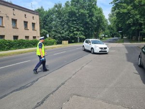 Umundurowany policjant zatrzymujący do kontroli pojazd osobowy.