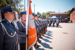 Zdjęcie kolorowe. Widoczny plac i uczestnicy uroczystości - umundurowani policjanci, na pierwszym planie poczet sztandarowy i sztandar