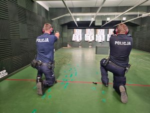 Umundurowani policjanci w postawie klęczącej podczas treningu strzeleckiego.