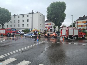 Miejsce zdarzenia drogowego.  W tle pojazdy osobowe uczestniczące w zdarzeniu oraz pojazdy Policji, Straży Pożarnej oraz Pogotowia Ratunkowego