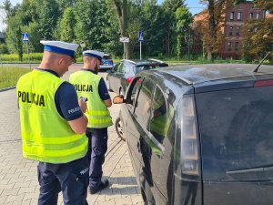 Dwaj umundurowani policjanci wydziału ruchu drogowego stojący przy pojeździe i przeprowadzający kontrolę drogową.