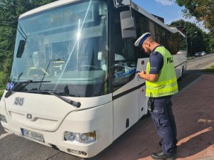 Umundurowany policjant wydziału ruchu drogowego stojący przy autobusie komunikacji miejskiej.