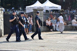 Idący umundurowani policjanci,  w oddali Wzgórze Kalwaryjskie oraz pielgrzymi