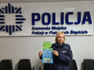 Umundurowana policjanta trzymająca w rękach podziękowanie przedstawiające żabę. Z tyłu napis &quot;Policja Komenda Miejska Policji w Piekarach Śląskich&quot;.