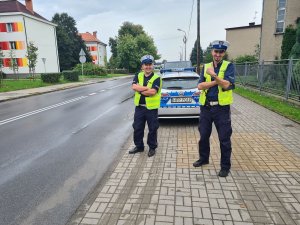 Umundurowani policjanci ruchu drogowego stojący obok policyjnego radiowozu