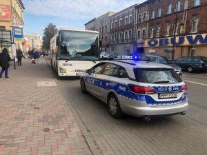 Oznakowany policyjny radiowóz stojący w zatoce autobusowej przed autobusem komunikacji miejskiej.