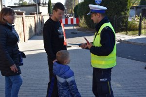 Umundurowany policjant wręczający mężczyźnie z dzieckiem ulotkę informacyjną
