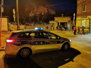 Zdjęcie nocą. Oznakowany policyjny radiowóz w rejonie cmentarza.