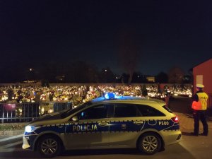 Zdjęcie nocą. Oznakowany policyjny radiowóz w rejonie cmentarza.