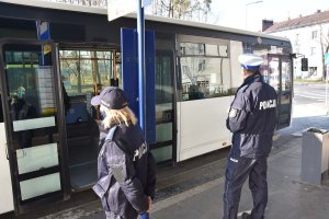 Policjanci stoją na przystanku komunikacji miejskiej. W tle autobus