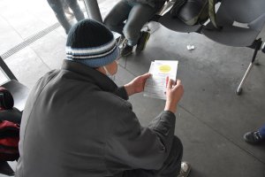 Mężczyzna siedzi na krześle w poczekalni dworca autobusowego i trzyma w rękach ulotkę wręczoną przez policjantów