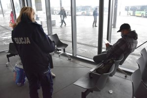Policjantka rozmawia z mężczyznami siedzącymi w poczekalni dworca autobusowego
