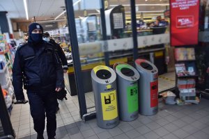 Policjant wraz ze strażnikiem miejskim kontrolują placówkę handlową pod kątem przestrzegania ograniczeń związanych z pandemią COVID-19.