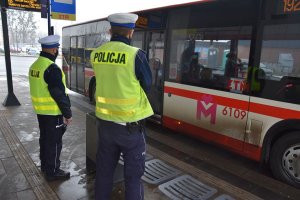 Policjanci wydziału ruchu drogowego stoją na przystanku komunikacji miejskiej obok autobusu