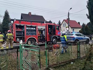 Wóz straży pożarnej oraz policyjny radiowóz podczas akcji gaśniczej. Z boku pojazdów stoją strażacy