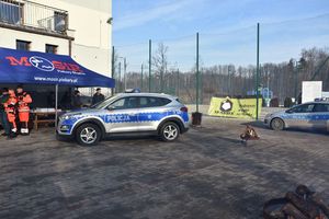 Oznakowane radiowozy na parkingu. Na kostce brukowej stoją paleniska. W tle namiot z Miejskiego Ośrodka Sportu i Rekreacji w Piekarach Śląskich