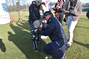 Pierwszy Zastępca Komendanta Miejskiego Policji w Piekarach Śląskich wręcza medal dziecku, które uczestniczyło w biegu. W tle inne osoby