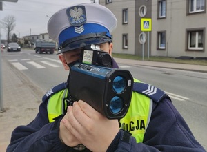 Umundurowany policjant kontrolujący prędkość pojazdów w rejonie oznakowanego przejścia dla pieszych.