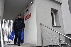 Umundurowana policjantka schodzi po schodach znajdujących się od frontu Komendy Miejskiej Policji w Piekarach Śląskich. Trzyma w rękach dwie torby z logo kampanii &quot;Nie Reagujesz Akceptujesz!&quot;