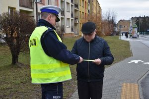 Umundurowany policjant w odblaskowej kamizelce wręcza mężczyźnie odblaskową opaskę.