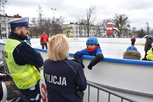 Umundurowani policjanci stoją obok lodowiska, z którego korzystają dzieci.