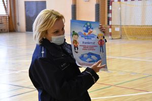 Umundurowana policjantka stoi na hali sportowej i trzyma w ręku plakat, na którym widnieją informacje &quot; Bezpieczna woda Pamiętaj wchodząc na zamarznięty zbiornik wodny zawsze ryzykujesz&quot;