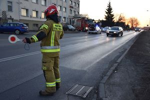 Strażak podczas regulacji ruchem. W tle pojazdy oraz budynek