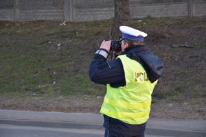 Umundurowany policjant ubrany w odblaskową kamizelkę fotografujący miejsce zdarzenia