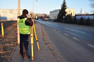 Umundurowany policjant w odblaskowej kamizelce z napisem policja obsługuje tachimetr na zdarzeniu drogowym